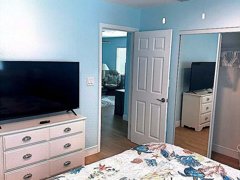 Furnished bedroom with ceiling fan, dresser and TV, plus a mirrored closet for convenient storage and easy organization.