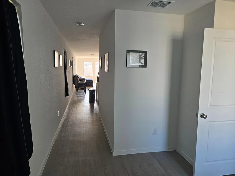 Long hallway with durable wood-look flooring and wall art leading to a furnished common area with natural light.