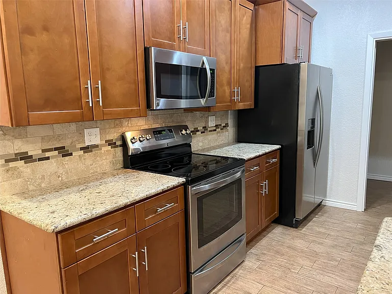 Kitchen featuring stainless steel appliances, wood cabinetry with brushed nickel hardware, light-toned countertops, and a tiled backsplash with decorative accents