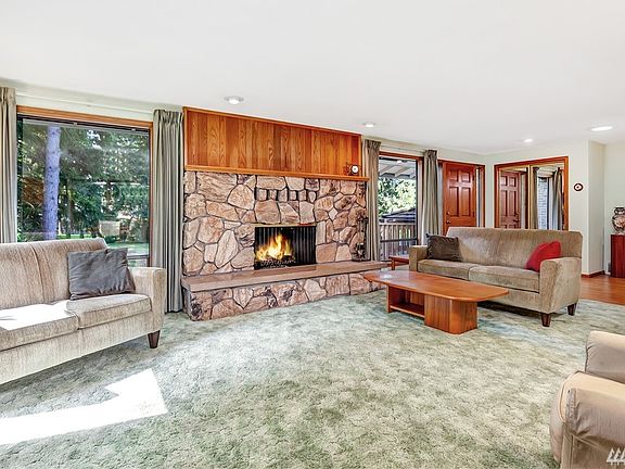 Living room has cozy wood fireplace, large windows overlooking front yard