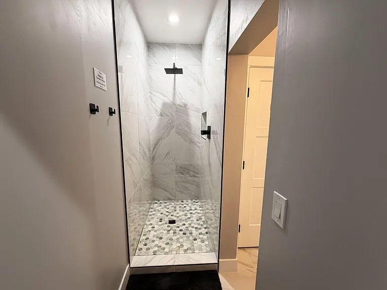 Walk-in shower with large-format tile walls, rainfall shower head, and mosaic tile flooring for easy maintenance