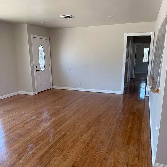 Living area from a second angle, highlighting refinished hardwood floors, fresh paint, and the front entry.