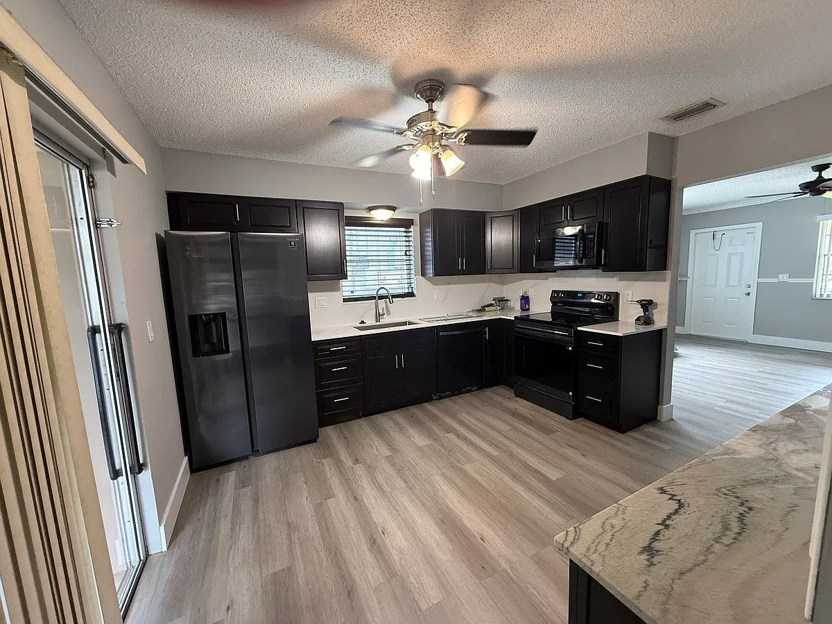 The kitchen has a modern, upscale look. Rich dark wood cabinetry is paired with sleek black appliances (refrigerator, stove, and microwave) for a clean, cohesive design. New quartz countertops and backsplash add a bright contrast and a high-end finish. - 243 SE 1st St