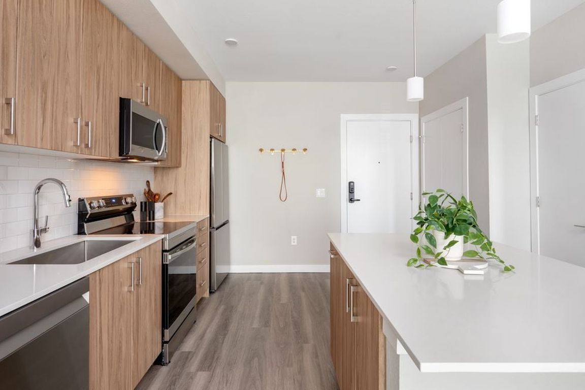 Finish Package II Kitchen with oak cabinetry, white quartz countertops, stainless steel appliances, pendant lighting, and hard-surface vinyl plank flooring