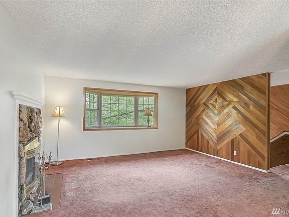 Upstairs living room with wood burning fireplace, large bay window, and geometric wood accents. 