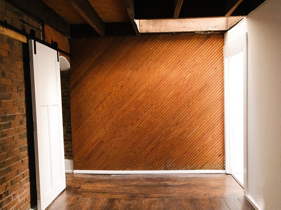Additional view of 2nd bedroom in back of unit and hallway that connects to the full bath in the apartment. Exposed brick and wood wall and hanging beams and skylight in top right of photo!