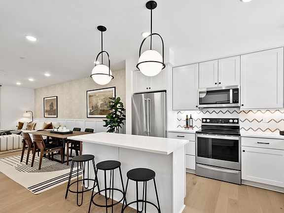A modern, open-concept kitchen and dining area with white cabinets, stainless steel appliances, and