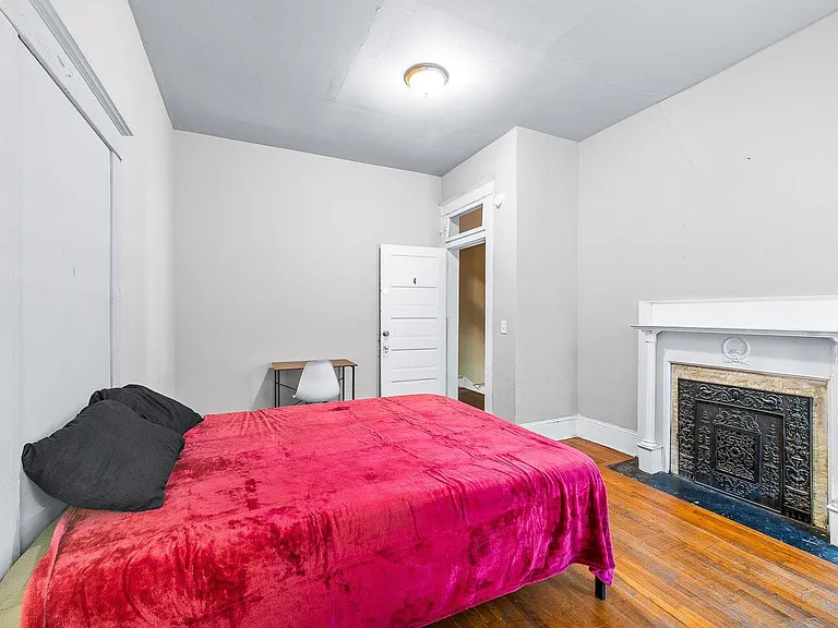 Bedroom with hardwood floors, a decorative fireplace mantel, and space for a bed plus a small desk or reading nook.