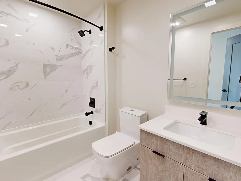 Apartment bathroom with tile flooring and LED vanity mirror.