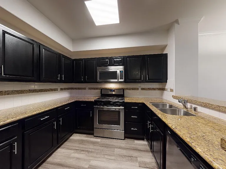 Apartment kitchen with stainless steel appliances, granite countertops and wood-style flooring.