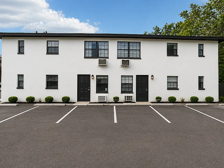 Contemporary white apartment building with black trim and ample parking space, set against a clear blue sky.