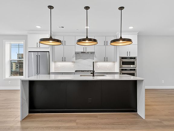 A modern, minimalist kitchen with sleek white cabinets, a black island, and three pendant lights han