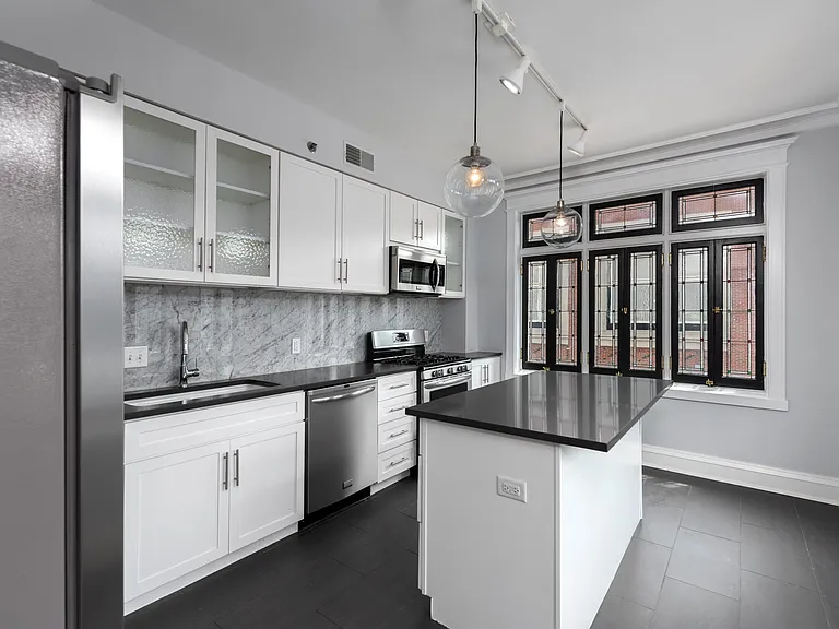 York House designer kitchen with gas stove, quartz countertops, stainless steel appliances, marble kitchen backsplash, and slate tile floor.