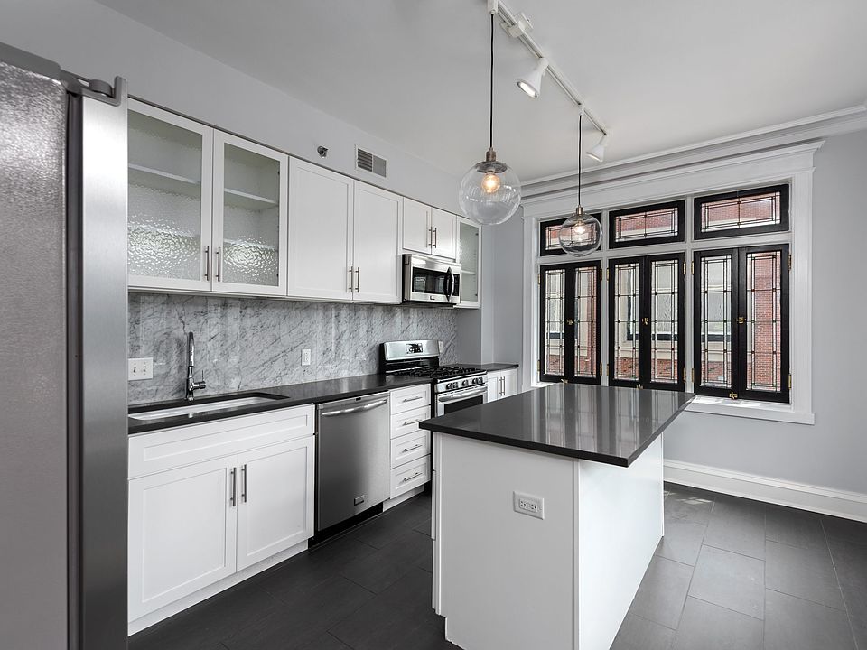 York House designer kitchen with gas stove, quartz countertops, stainless steel appliances, marble kitchen backsplash, and slate tile floor.