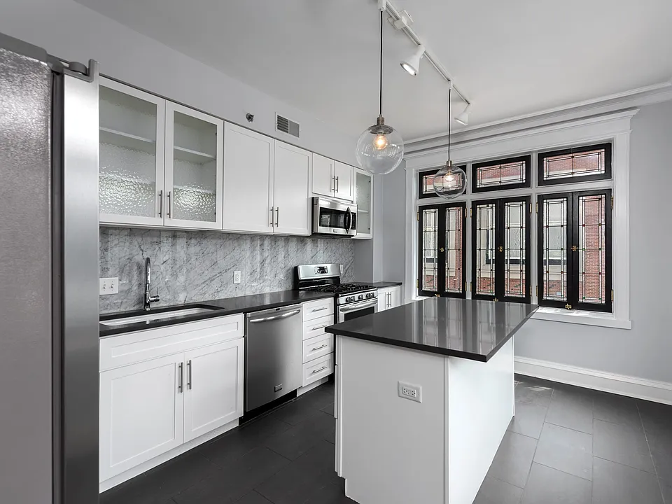 York House designer kitchen with gas stove, quartz countertops, stainless steel appliances, marble kitchen backsplash, and slate tile floor.