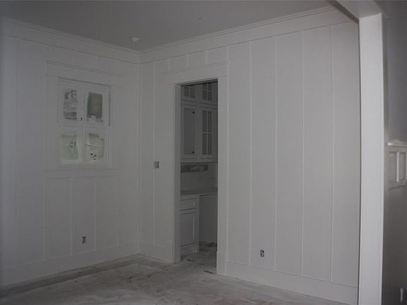 Formal dining at front of home has beautiful board and batt full wall trim, with butler pantry beyond