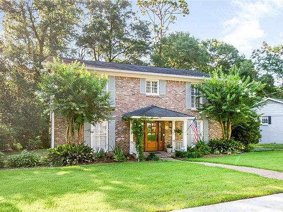 Two-story brick facade residence featuring a covered front porch with white columns, a natural wood entry door, and light blue window shutters