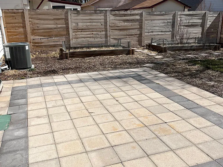 Back yard paver patio with raised garden beds in background.