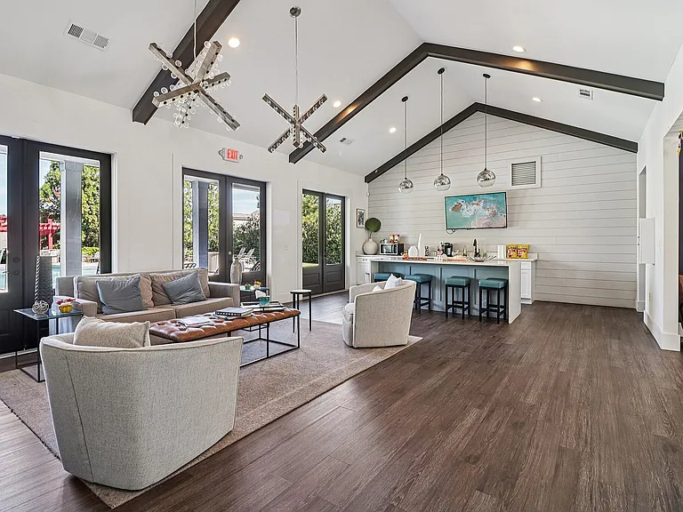 Elegant open-concept clubhouse with vaulted ceilings, featuring modern lighting, cozy seating, and a chic kitchen with bar stools and stylish decor.
