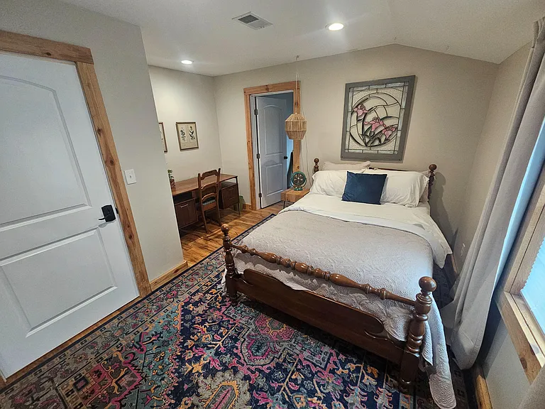 Furnished bedroom with a full bed, wood floors, area rug, and a dedicated desk nook with storage for work or study.