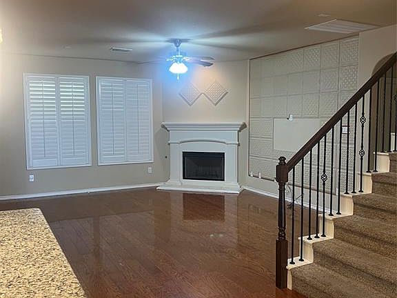 Unfurnished living room featuring a fireplace with raised hearth, dark wood-style floors, stairs, and a ceiling fan