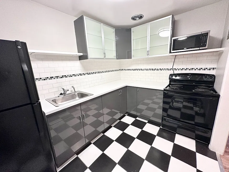 Modern kitchen with sleek black and white cabinetry, chic checkered floor, and contemporary appliances.