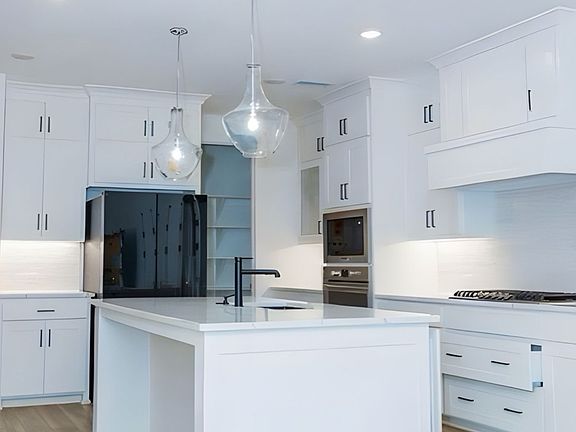 Kitchen featuring light wood finished floors, white cabinets, light countertops, a center island with sink, and tasteful backsplash