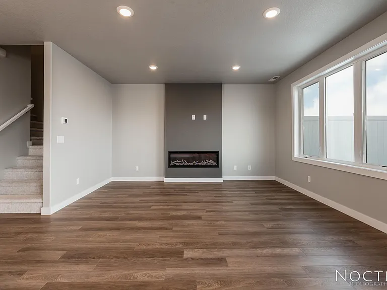 Living room with electric fireplace off the open kitchen and dining space. (Photo of another unit with similar finishes and quality.)