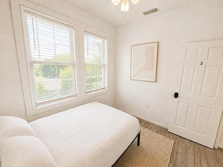 Private bedroom with two large windows, ceiling fan, and durable flooringideal for resting and everyday storage needs.