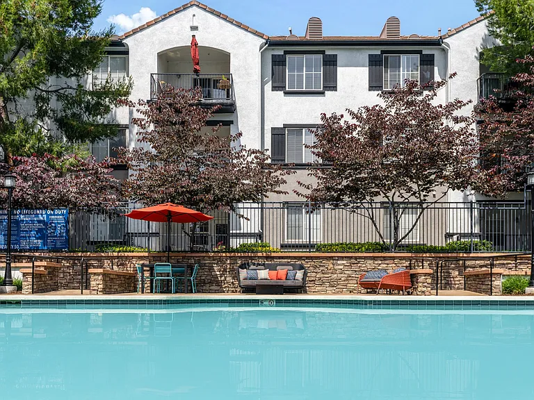 Community Pool Surrounded by Trees, Loungers, and Umbrella Tables