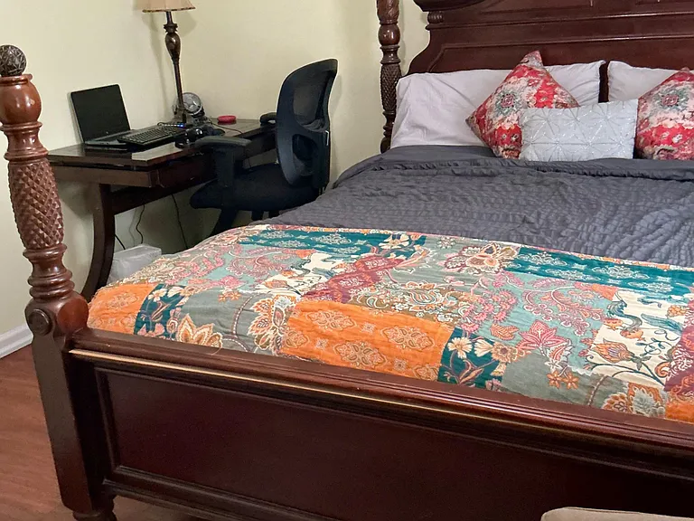 Furnished bedroom featuring a carved four-poster bed, area rug, and a dedicated desk setup for work or study.