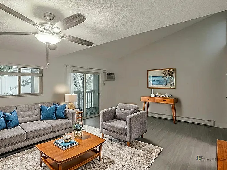Bright and inviting living room with cozy gray sofas, modern ceiling fan, and sliding doors leading to a picturesque balcony.