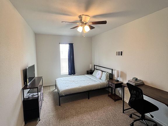 Furnished bedroom with a full bed, nightstands, desk workspace, and a TV stand, plus a window and ceiling fan.