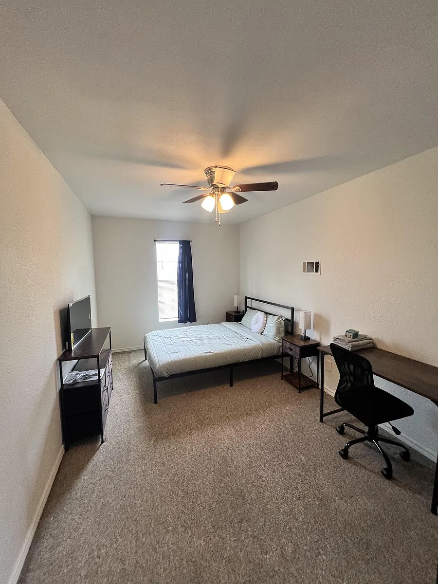 Furnished bedroom with a full bed, nightstands, desk workspace, and a TV stand, plus a window and ceiling fan. - Archwood St