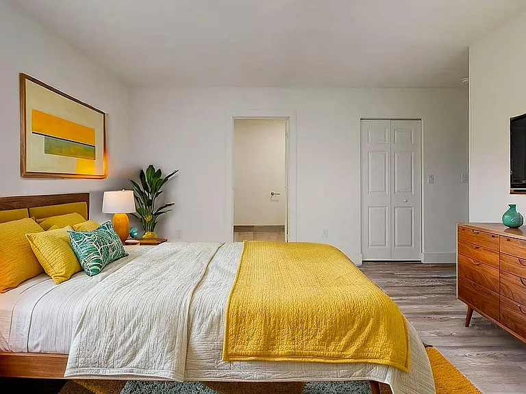 Bright and inviting bedroom with contemporary decor, featuring a cozy bed with vibrant yellow accents, stylish wooden furniture, and modern art on the wall.