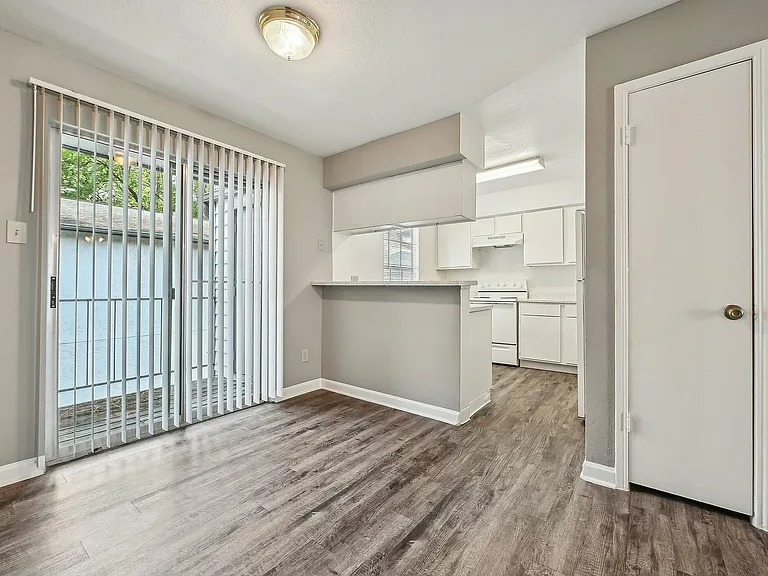 Bright and modern kitchen with sleek white cabinetry, an inviting breakfast bar, and elegant hardwood floors opening to a sunlit patio at Driscoll Place.