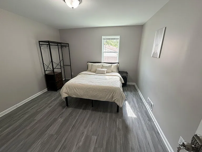 Private bedroom with wood-look flooring, a window for natural light, and space for storage with a clothes rack and nightstand