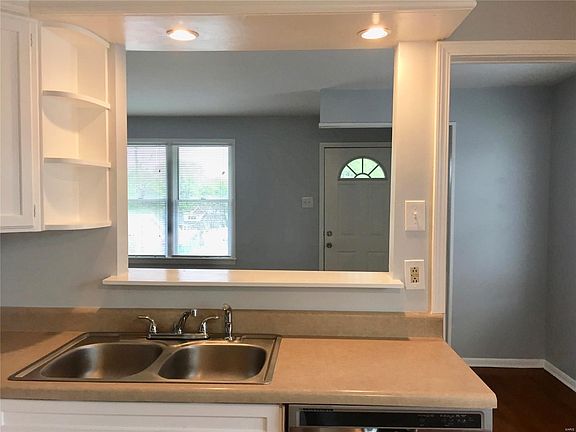 South facing view of kitchen sink overlooking the living room and front door. Display shelving above sink.