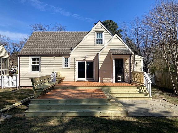 Large back deck with two levels and built-in seating, plus a stone patio, lead to a large fenced-in back yard.