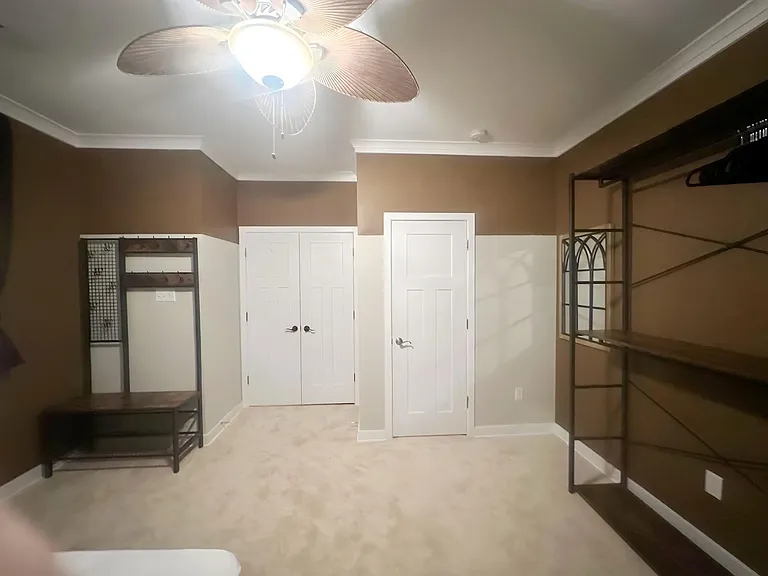 Spacious bedroom with carpeted floors, ceiling fan, and built-in shelving plus a large closet for easy storage.