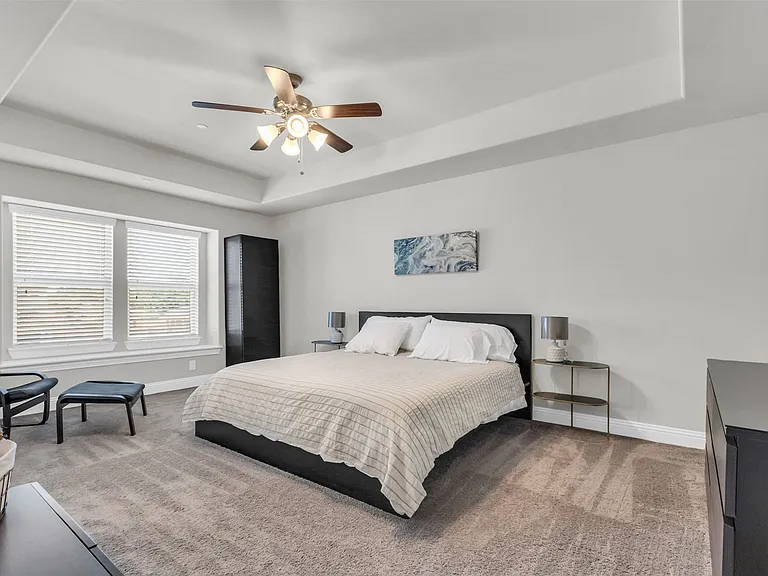 Spacious carpeted room featuring a tray ceiling with a ceiling fan, dual windows with blinds, and light gray wall paint