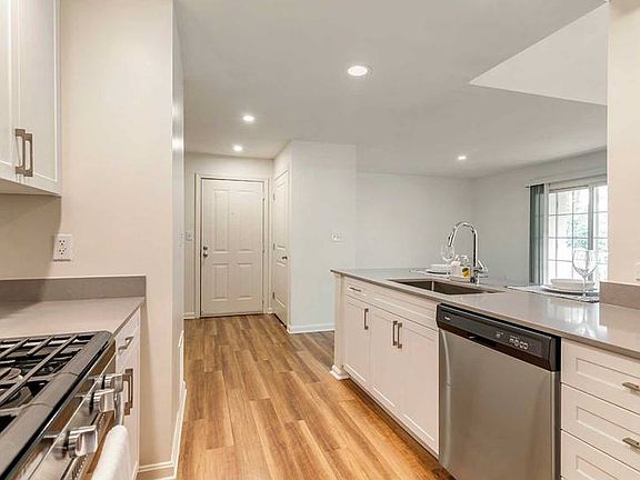 Newly renovated Finish Package II kitchen with white cabinetry, grey quartz countertops, grey tile backsplash, stainless steel appliances, and hard surface flooring