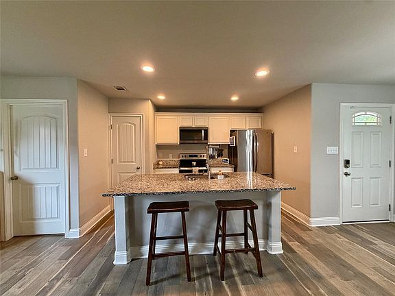 Kitchen featuring an island with bar seating, stone-finish countertop, stainless steel appliances, recessed lighting, and wood-finish flooring