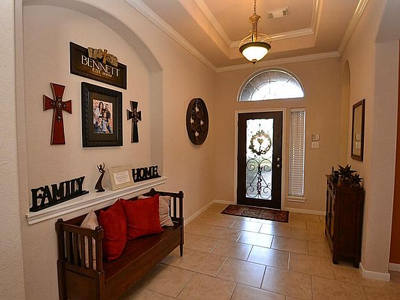 Elegant entry offering a glass front door with iron rail accents, tile flooring, tiered ceilings and double crown molding.