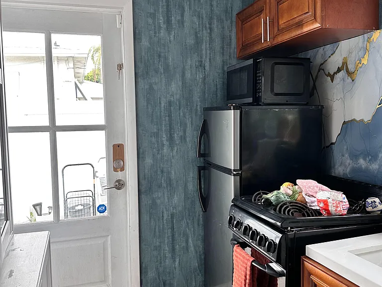 Compact kitchen with range, microwave, and upper cabinets, plus a glass-panel door for easy access and ventilation.
