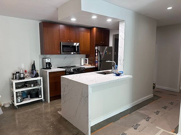 Newly remodeled open kitchen with porcelain waterfall countertops and stainless-steel appliances. (Please disregard the construction)