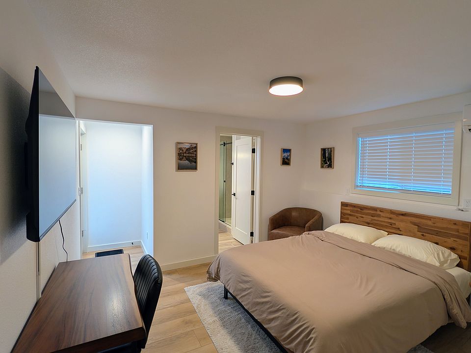 Shows the queen size bed, entrance to the bathroom, the small hallway to the exterior entrance. As well as the dedicated workspace and the smart TV.