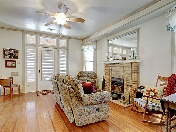 Living room with fireplace on the right in an extended bay window of the house. Fireplace has decorative mock heater. Crown molding, tall baseboards and refinished floors. Note the transoms and wide sidelights in the doorway.