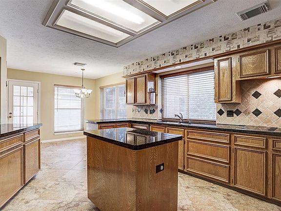 ISLAND KITCHEN WITH GRANITE COUNTERS, TRAVERTINE TILE BACKSPLASH AND 18" TILE FLOORS.