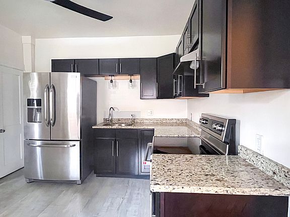 The kitchen blends charm and functionality with modern Cortec flooring, espresso-colored Shaker cabinets, granite countertops, and large west-facing windows that fill the space with natural light. Modern stainless steel appliances.